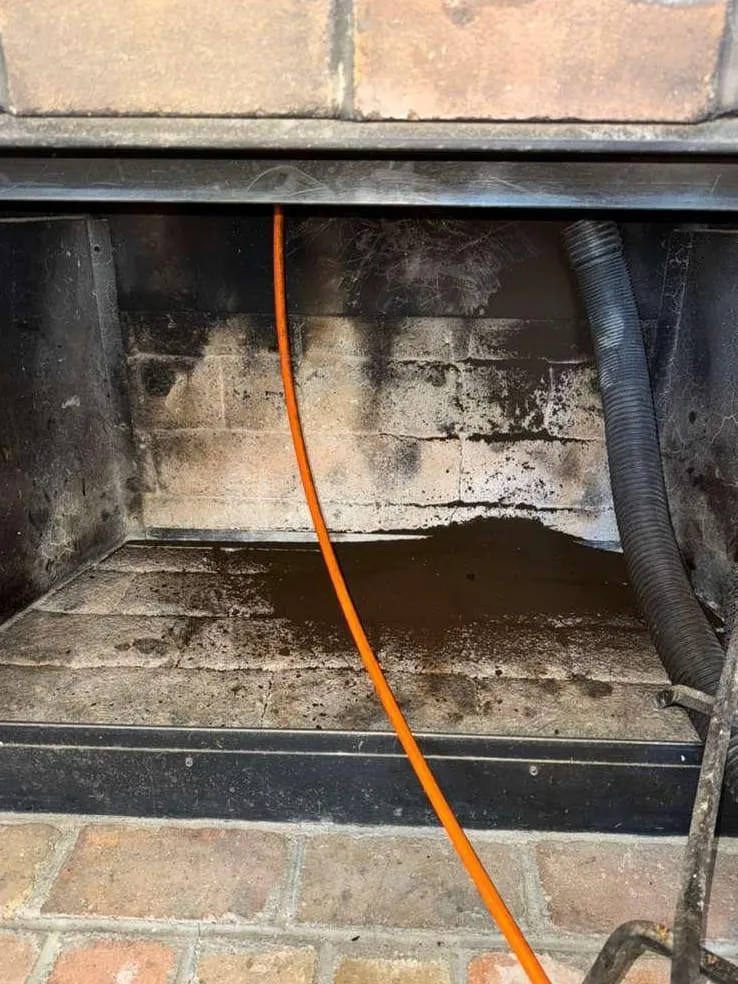 A brick firebox with soot on its walls, an orange cable hanging down the middle and a ribbed vacuum hose on the right